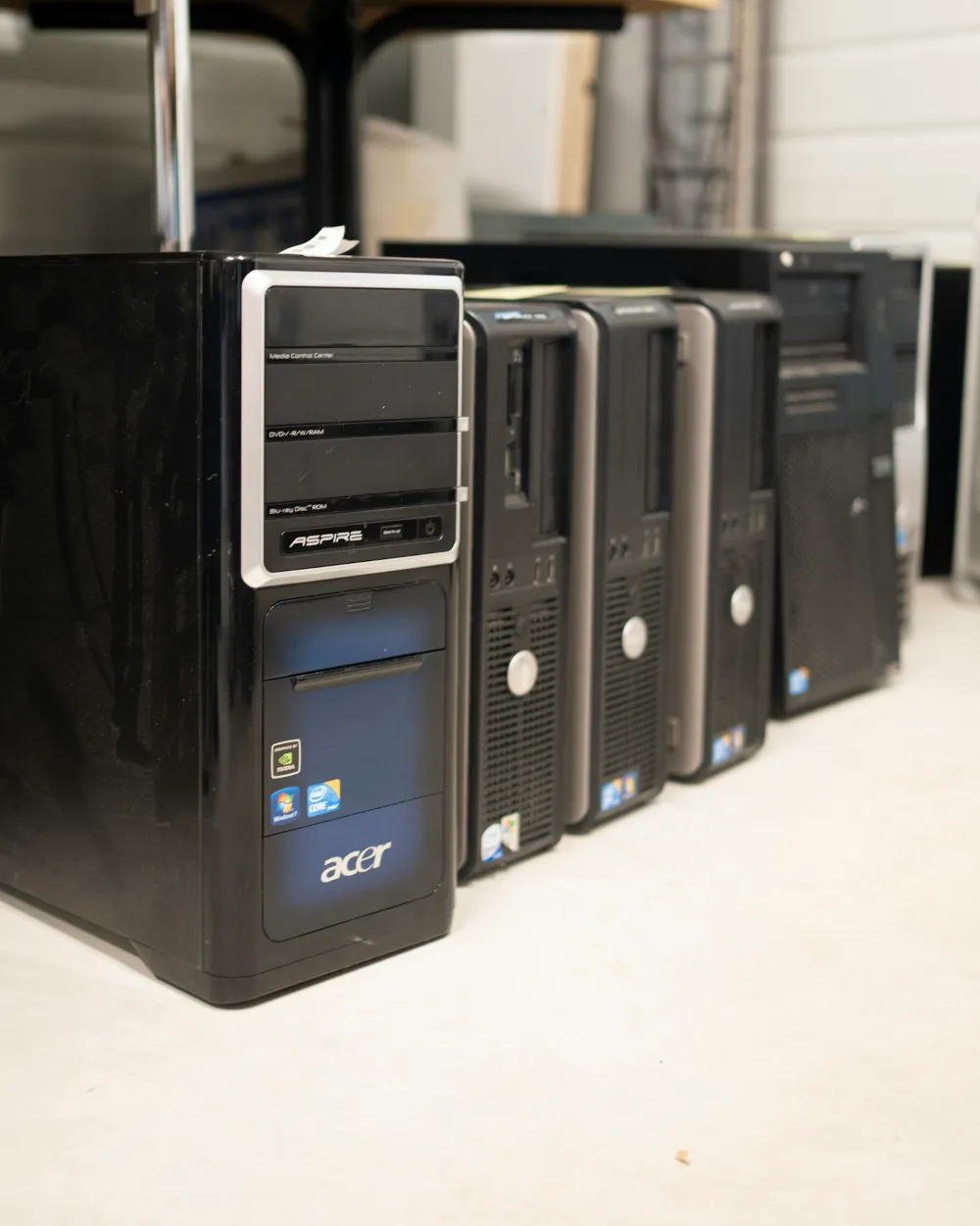 Computadores de secretária usados, alinhados no chão junto a uma parede.
